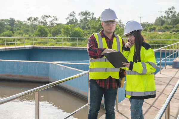 Environmental engineers working at wastewater treatment plant, technicians discussing work together.