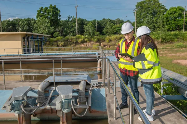 Environmental engineers working at wastewater treatment plant, technicians discussing work together.