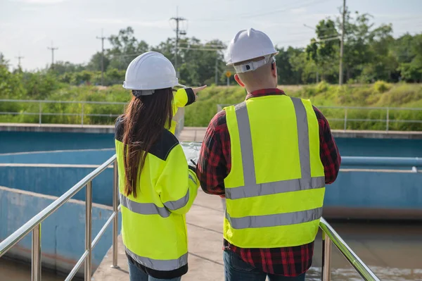 Environmental engineers working at wastewater treatment plant, technicians discussing work together.