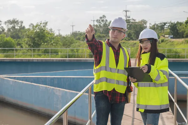 Environmental engineers working at wastewater treatment plant, technicians discussing work together.