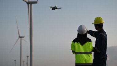 Taylandlı, dağdaki rüzgar türbini çiftliği güç jeneratörü istasyonunda çalışan ve raporu tutan iki mühendis, teknisyen ve kadın iş hakkında konuşuyor, yüksek açılı drone görüşü kullanıyorlar.