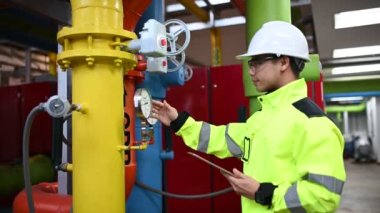 Kazan dairesinde çalışan gözlüklü Asyalı mühendis, ısıtma sistemi ekipmanlarının teknik verilerini kontrol ediyor, Taylandlılar