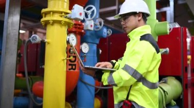 Kazan dairesinde çalışan gözlüklü Asyalı mühendis, ısıtma sistemi ekipmanlarının teknik verilerini kontrol ediyor, Taylandlılar