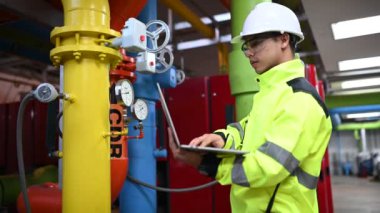 Kazan dairesinde çalışan gözlüklü Asyalı mühendis, ısıtma sistemi ekipmanlarının teknik verilerini kontrol ediyor, Taylandlılar