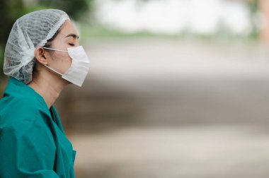 Depresyonda olan Asyalı kadın hemşire yüz maskesi giyiyor mavi üniforma hastane zemininde oturuyor, genç kadın doktor sıkı çalışmaktan strese giriyor.