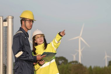 Taylandlı iki mühendis rüzgar türbini çiftliği güç jeneratörü istasyonunda çalışıyor ve raporları tutuyor. Teknisyen erkek ve kadın iş hakkında tartışıyorlar.