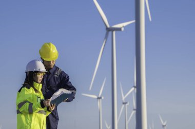 Taylandlı iki mühendis rüzgar türbini çiftliği güç jeneratörü istasyonunda çalışıyor ve raporları tutuyor. Teknisyen erkek ve kadın iş hakkında tartışıyorlar.