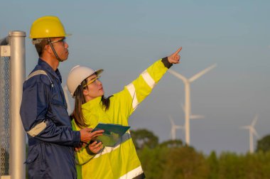 Taylandlı iki mühendis rüzgar türbini çiftliği güç jeneratörü istasyonunda çalışıyor ve raporları tutuyor. Teknisyen erkek ve kadın iş hakkında tartışıyorlar.