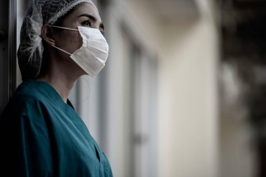 Depresyonda olan Asyalı kadın hemşire yüz maskesi giyiyor mavi üniforma hastane zemininde oturuyor, genç kadın doktor sıkı çalışmaktan strese giriyor.