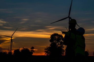 Taylandlı iki mühendis rüzgar türbini çiftliği güç jeneratörü istasyonunda çalışıyor ve raporları tutuyor. Teknisyen erkek ve kadın iş hakkında tartışıyorlar.