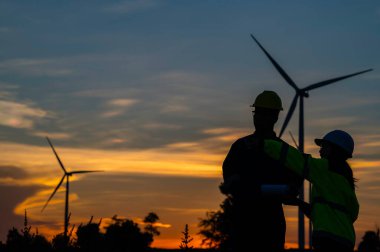 Taylandlı iki mühendis rüzgar türbini çiftliği güç jeneratörü istasyonunda çalışıyor ve raporları tutuyor. Teknisyen erkek ve kadın iş hakkında tartışıyorlar.