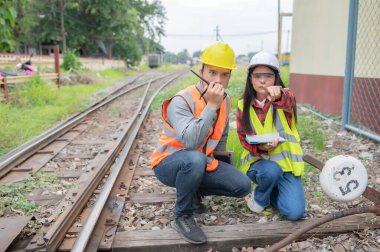 Tren istasyonunda çalışan iki mühendis, birlikte mutlu bir şekilde çalışıp, sorunu çözümlemede birbirlerine yardım edip, gelişim yönergelerine danışırlar.