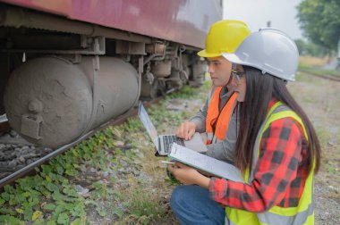 Tren istasyonunda çalışan iki mühendis, birlikte mutlu bir şekilde çalışıp, sorunu çözümlemede birbirlerine yardım edip, gelişim yönergelerine danışırlar.