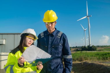 Taylandlı iki mühendis rüzgar türbini çiftliği güç jeneratörü istasyonunda çalışıyor ve raporları tutuyor. Teknisyen erkek ve kadın iş hakkında tartışıyorlar.