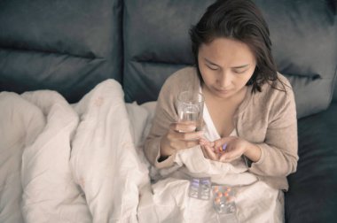 Asyalı hasta kadın kanepede oturur, evde oturur, kadın kendini kötü hisseder, uzanmak ve dinlenmek ister, yüksek ateş, covid-19 omikron gerilimi