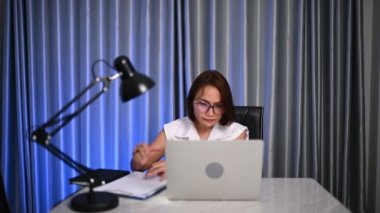 Güzel Asyalı kadın gece evde çalışıyor, şirketten bir sürü iş, eve iş getiriyor, ev konseptinden çalışıyor, sıkı çalışmaktan yorulmuş.