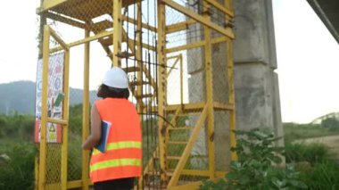 Otoyol köprüsü şantiyesinde çalışan Asyalı bir kadın mühendis inşaat çalışmalarını denetliyor.