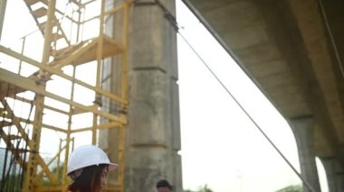 Otoyol köprüsü şantiyesinde çalışan Asyalı bir kadın mühendis inşaat çalışmalarını denetliyor.