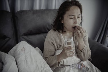 Asyalı hasta kadın kanepede oturur, evde kalır, kadın kendini kötü hisseder, uzanıp dinlenmek ister, yüksek ateş.