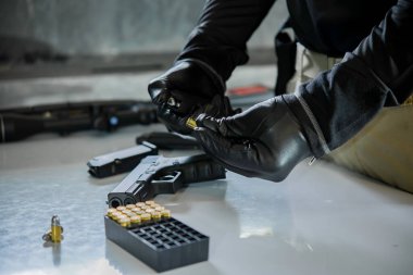 Elinde silahla siyah deri eldivenler giyen Asyalı bir erkek silaha kurşun dolduruyor.