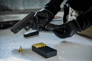 Elinde silahla siyah deri eldivenler giyen Asyalı bir erkek silaha kurşun dolduruyor.