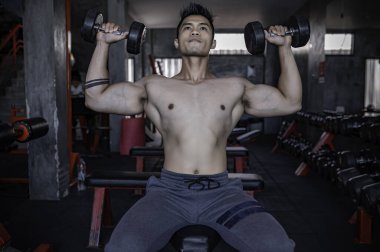 Spor salonunda çalışan yakışıklı, ağırlık kaldıran Asyalı bir adam spor müsabakası için ağırlık kaldırıyor sırt kası çalıştırmak için halteri kaldırıyor.