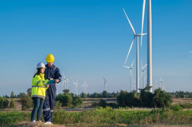 Taylandlı iki mühendis rüzgar türbini çiftliği güç jeneratörü istasyonunda çalışıyor ve raporları tutuyor. Teknisyen erkek ve kadın iş hakkında tartışıyorlar.