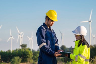 Taylandlı iki mühendis rüzgar türbini çiftliği güç jeneratörü istasyonunda çalışıyor ve raporları tutuyor. Teknisyen erkek ve kadın iş hakkında tartışıyorlar.