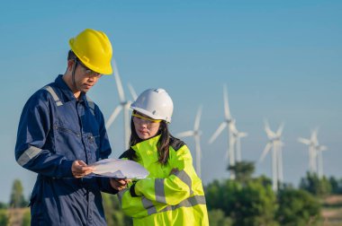 Taylandlı iki mühendis rüzgar türbini çiftliği güç jeneratörü istasyonunda çalışıyor ve raporları tutuyor. Teknisyen erkek ve kadın iş hakkında tartışıyorlar.