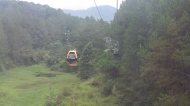 Dağlardaki yeşil ormanın üzerinden geçen kablo araba.