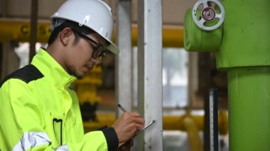 Kazan dairesinde çalışan gözlüklü Asyalı mühendis, ısıtma sistemi ekipmanlarının teknik verilerini kontrol ediyor, Taylandlılar