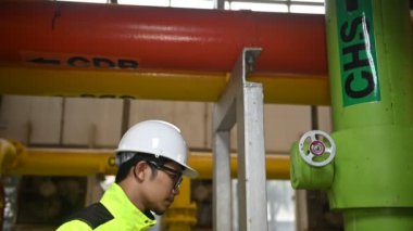 Kazan dairesinde çalışan gözlüklü Asyalı mühendis, ısıtma sistemi ekipmanlarının teknik verilerini kontrol ediyor, Taylandlılar