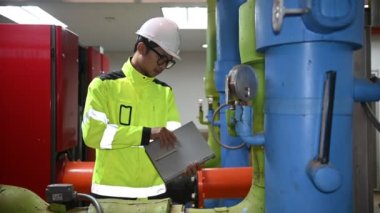 Kazan dairesinde çalışan gözlüklü Asyalı mühendis, ısıtma sistemi ekipmanlarının teknik verilerini kontrol ediyor, Taylandlılar