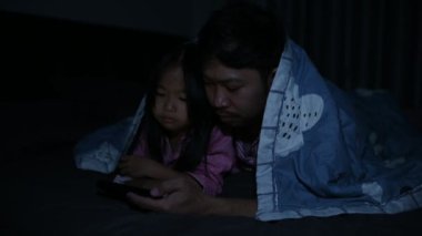 Baba ve kızı yatak odasında uyur, telefonlu çizgi film izler, Babalar Günü konsepti, bekar baba, uyumadan önce masal dinler.