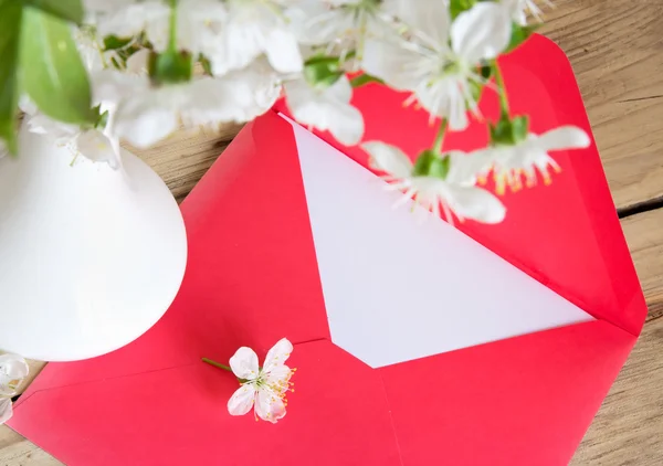 Enveloppe rouge et vase blanc de fleurs de cerisier sur fond de bois — Photo