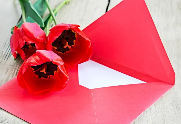 Red bouquet of tulips & envelope on wooden background. — Stock Photo, Image