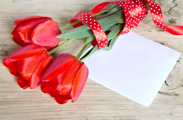 Bouquet de tulipes rouges et feuille de papier sur fond en bois . — Photo