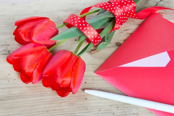 Buquê de tulipas vermelhas e envelope fundo de madeira . — Fotografia de Stock