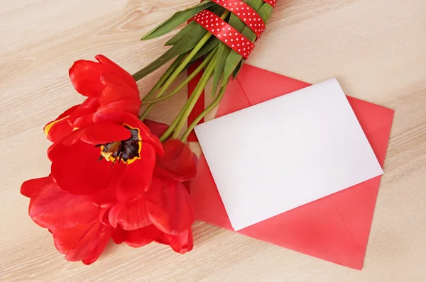 Bouquet de tulipes rouges avec carte de papier blanc et enveloppe sur table en bois — Photo