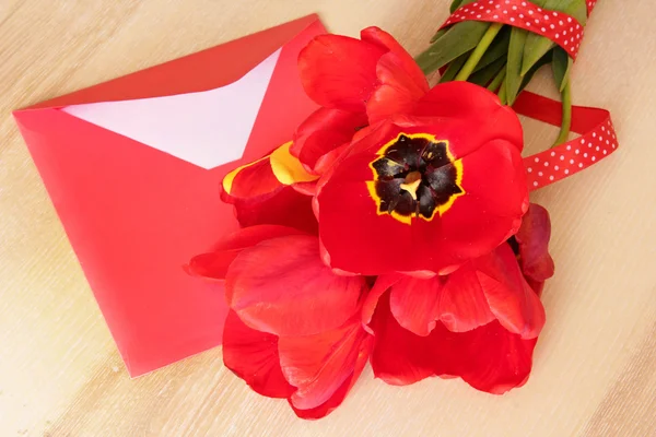 Bouquet of red tulips & envelope with pen on wooden background. — Stock Photo, Image