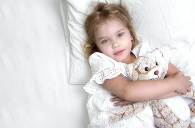 Child girl in bed holding toy empty white copy space.Little girl top view portrait. Caucasian kid health care and hygiene concept.Beautiful toddler.