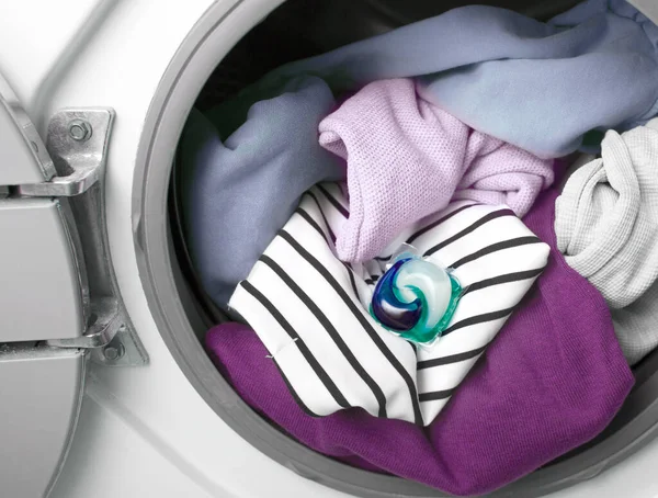 Laundry in wash machine with gel washing pod. Laundry washing capsule. Liquid detergent.
