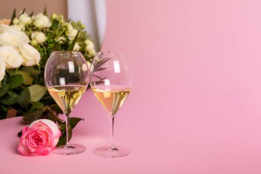 Güzel güller ve pembe arka planda iki bardak beyaz şarap. Sevgililer Günü için çiçek ve şaraplı romantik kompozisyon veya romantik aşk yemeği. Çiçekli ve şarap kadehli düğün kartı. Romantik ruh hali ve atmosfer. Fransız beyaz şarabı..