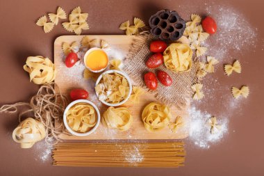Kahverengi arka planda, kırsal tarzda lezzetli İtalyan makarnası manzarası. Spagetti, fettuccine, farfalle ve ahşap masada kiraz domatesleri. Düz yerde yemek vardı. Kahverengi arka planda kırsal tarzda iştah açıcı makarna. Çiğ pasta. Geleneksel yemek..
