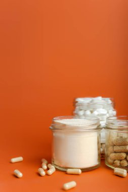 Besin takviyeleri, bir bardak su ve C vitamini, magnezyum, A vitamini, protein, elektrolit ve kolajen peptidleri gibi çeşitli vitaminler turuncu parlak arka planda güzel bileşimlerde bulunur.. 