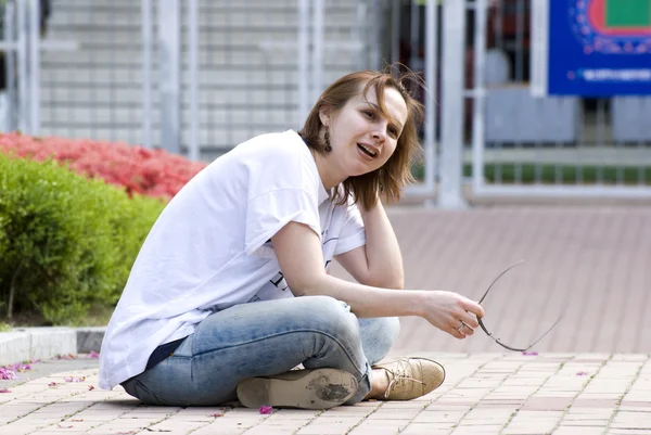 Young girl of the European appearance sitting on the sidewalk . — Stock Photo, Image