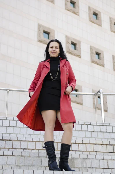 Young beautiful girl in a black dress and a red raincoat .