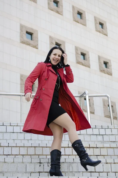 Young beautiful girl in a black dress and a red raincoat .