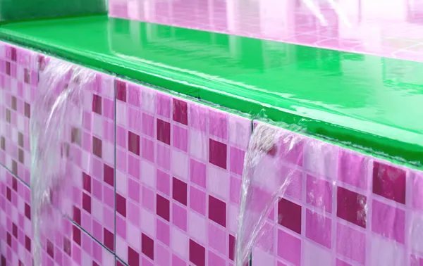 Closeup overflowing water of vibrant green and magenta pink tiled swimming pool spillway