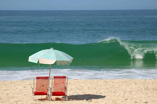 在沙滩上铺着阳伞的红色沙滩空椅子 与汹涌的大西洋波涛相映成趣 — 图库照片